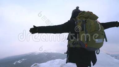 一个年轻人，一个游客，站在一座白雪覆盖的山的边缘，欣赏山顶。